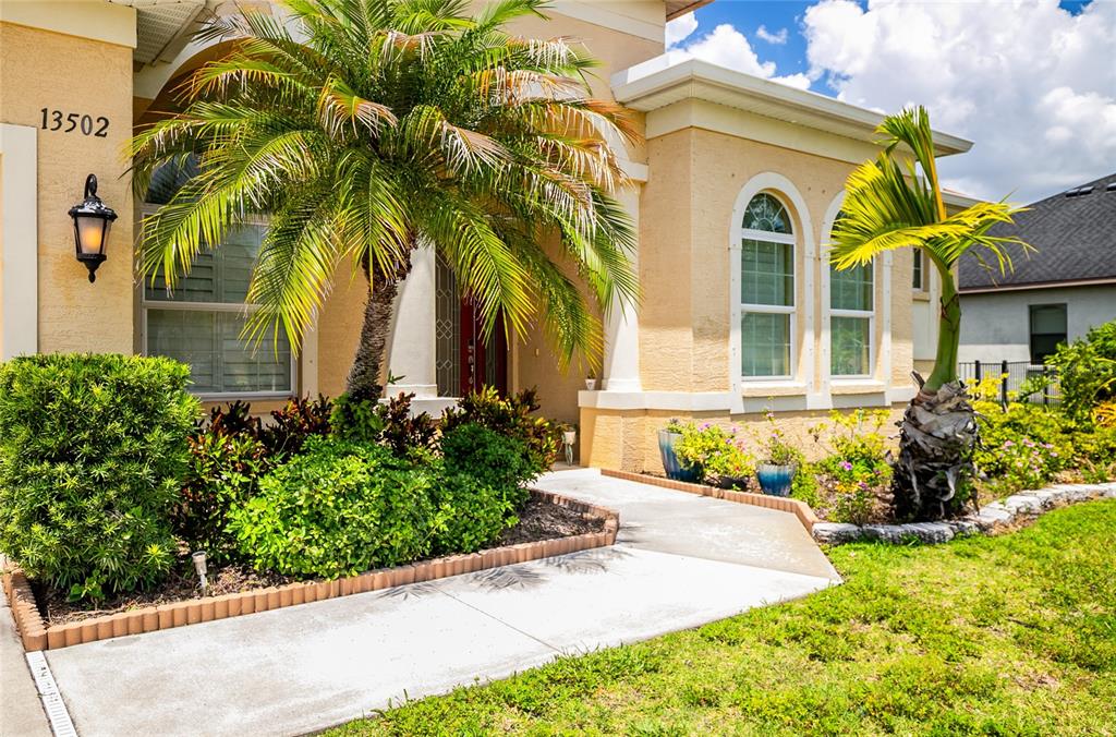 A concrete walkway leads to the front entrance of a tan house with palm trees — 13502 22ND COURT E, PARRISH, FL