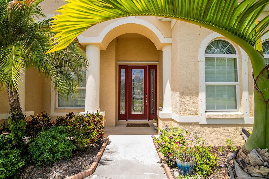 The front entrance of a house features a red door, white columns, and palm trees — 13502 22ND COURT E, PARRISH, FL
