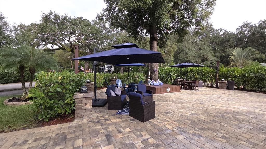 A paved outdoor patio features wicker furniture, blue umbrellas, and a raised wooden platform — 332 BOBCAT LANE, LAKE WALES, FL