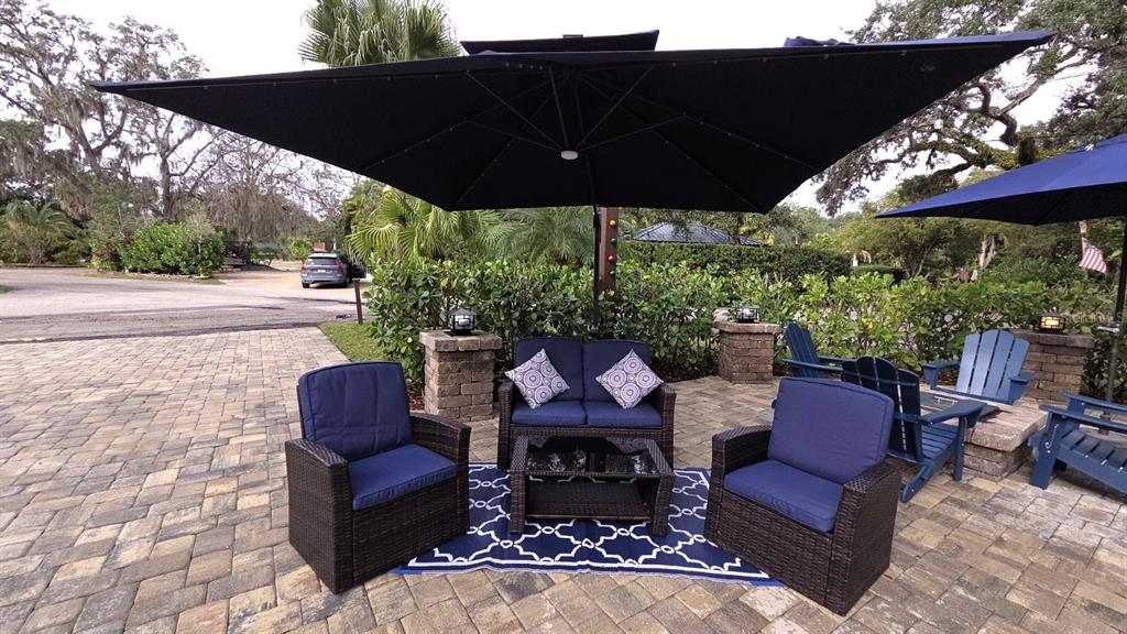 An outdoor patio features wicker furniture with blue cushions under a large black umbrella — 332 BOBCAT LANE, LAKE WALES, FL