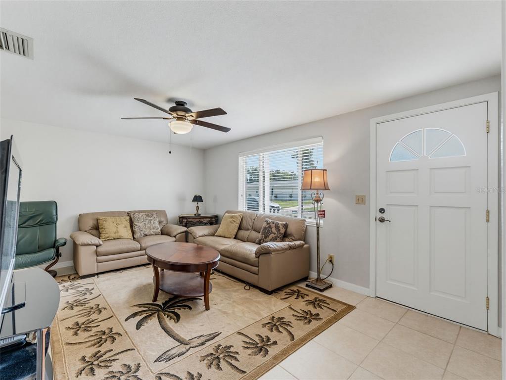A living room features beige sofas, a palm tree area rug, and a white front door — 4737 BELFAST DRIVE, NEW PORT RICHEY, FL