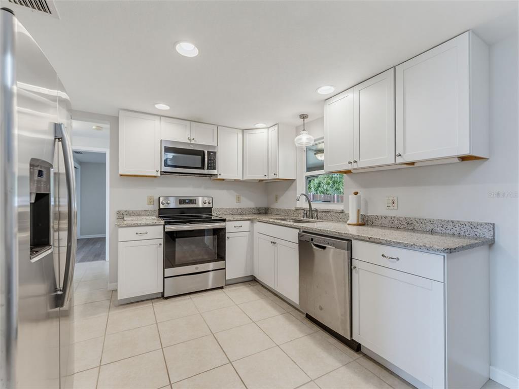 A kitchen with white cabinets, granite countertops, stainless steel appliances, and light-colored tile flooring — 4737 BELFAST DRIVE, NEW PORT RICHEY, FL