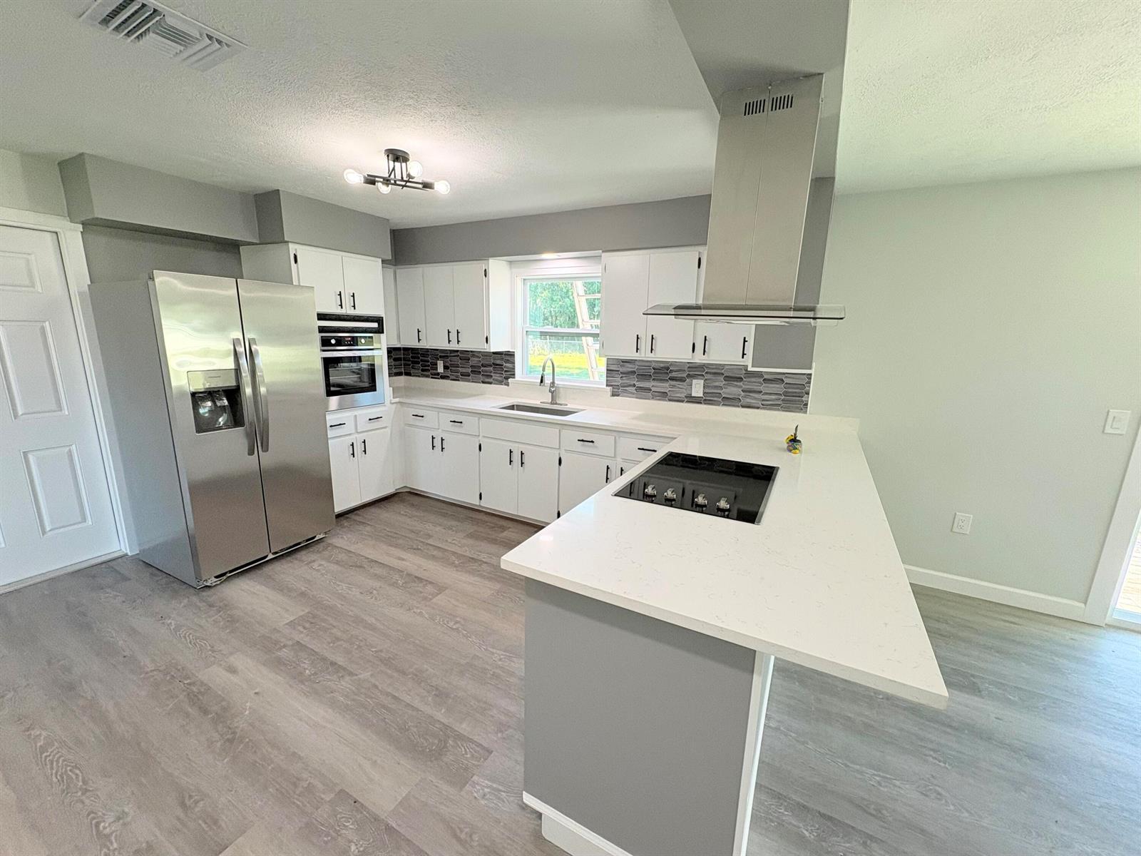 A kitchen with white cabinets, stainless steel appliances, a gray backsplash, and a quartz island — 2618 SE 38th Trail, Okeechobee FL 34974, OKEECHOBEE, FL