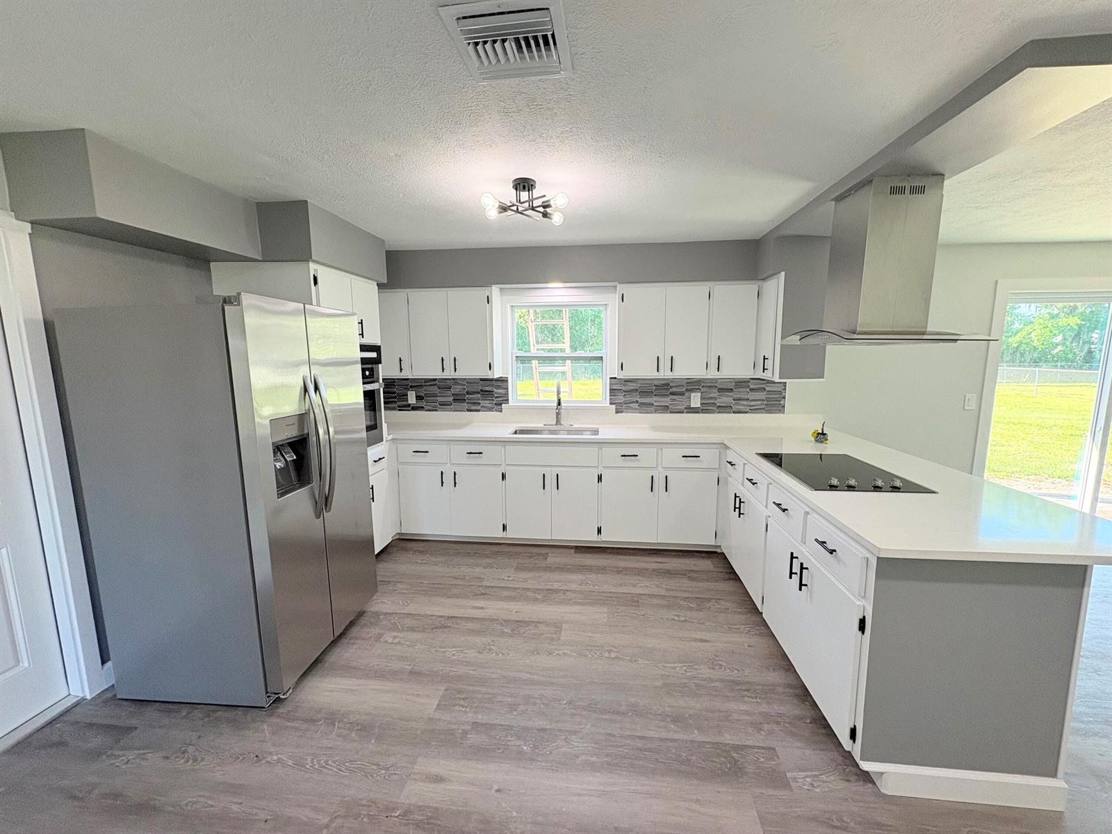 A kitchen features white cabinets, stainless steel appliances, a gray backsplash, and light wood flooring — 2618 SE 38th Trail, Okeechobee FL 34974, OKEECHOBEE, FL