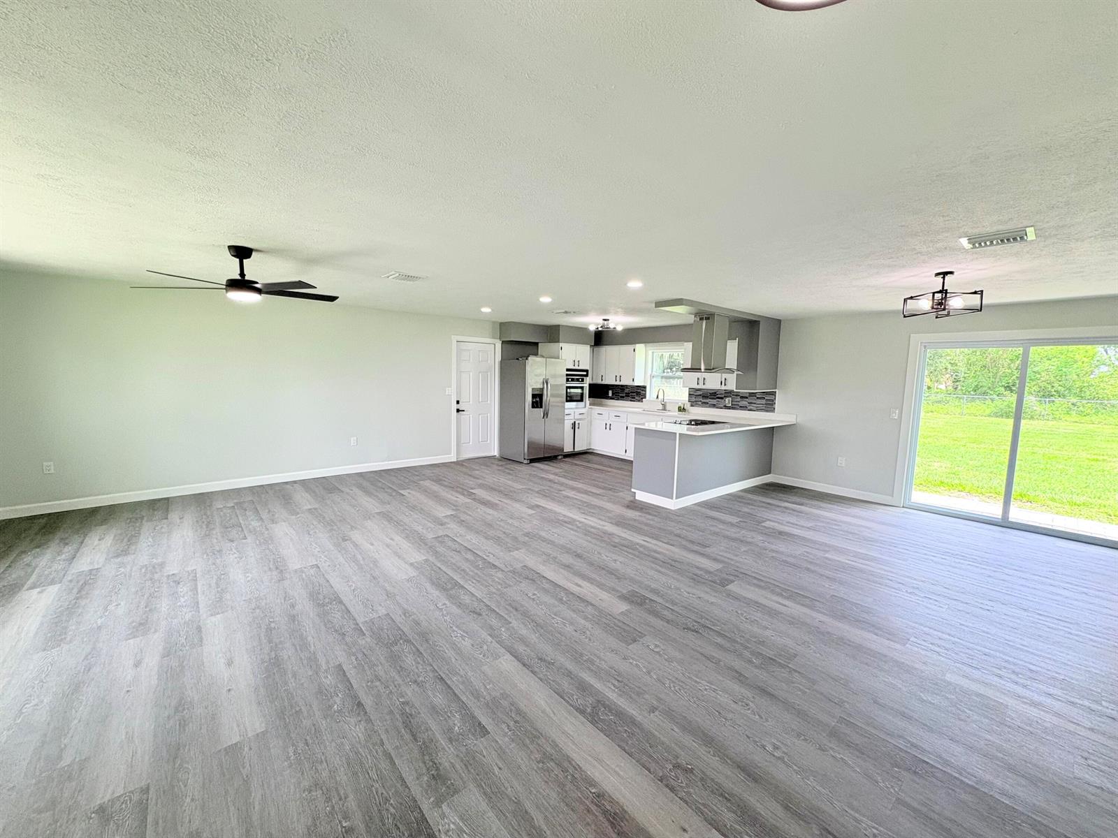 An open-concept kitchen and living area features gray wood-look flooring and white cabinetry — 2618 SE 38th Trail, Okeechobee FL 34974, OKEECHOBEE, FL
