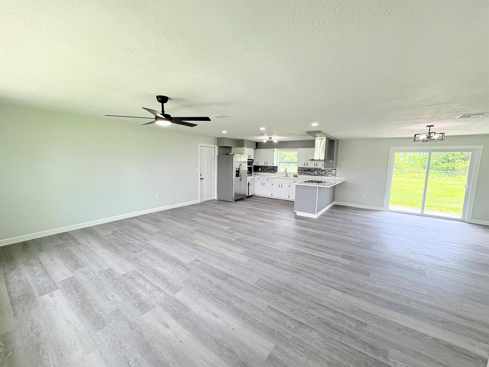 An open-concept living area features light gray wood-look flooring, a kitchen, and sliding glass doors — 2618 SE 38th Trail, Okeechobee FL 34974, OKEECHOBEE, FL