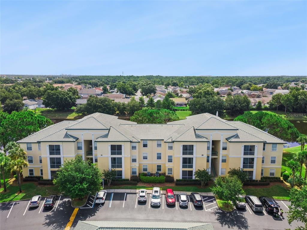 An aerial view shows a multi-story apartment building with a parking lot in the foreground — 8811 DUNES COURT UNIT 308, KISSIMMEE, FL