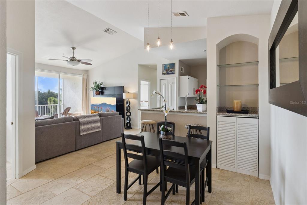 A dining area with a dark table and chairs sits adjacent to an open living room — 8811 DUNES COURT UNIT 308, KISSIMMEE, FL