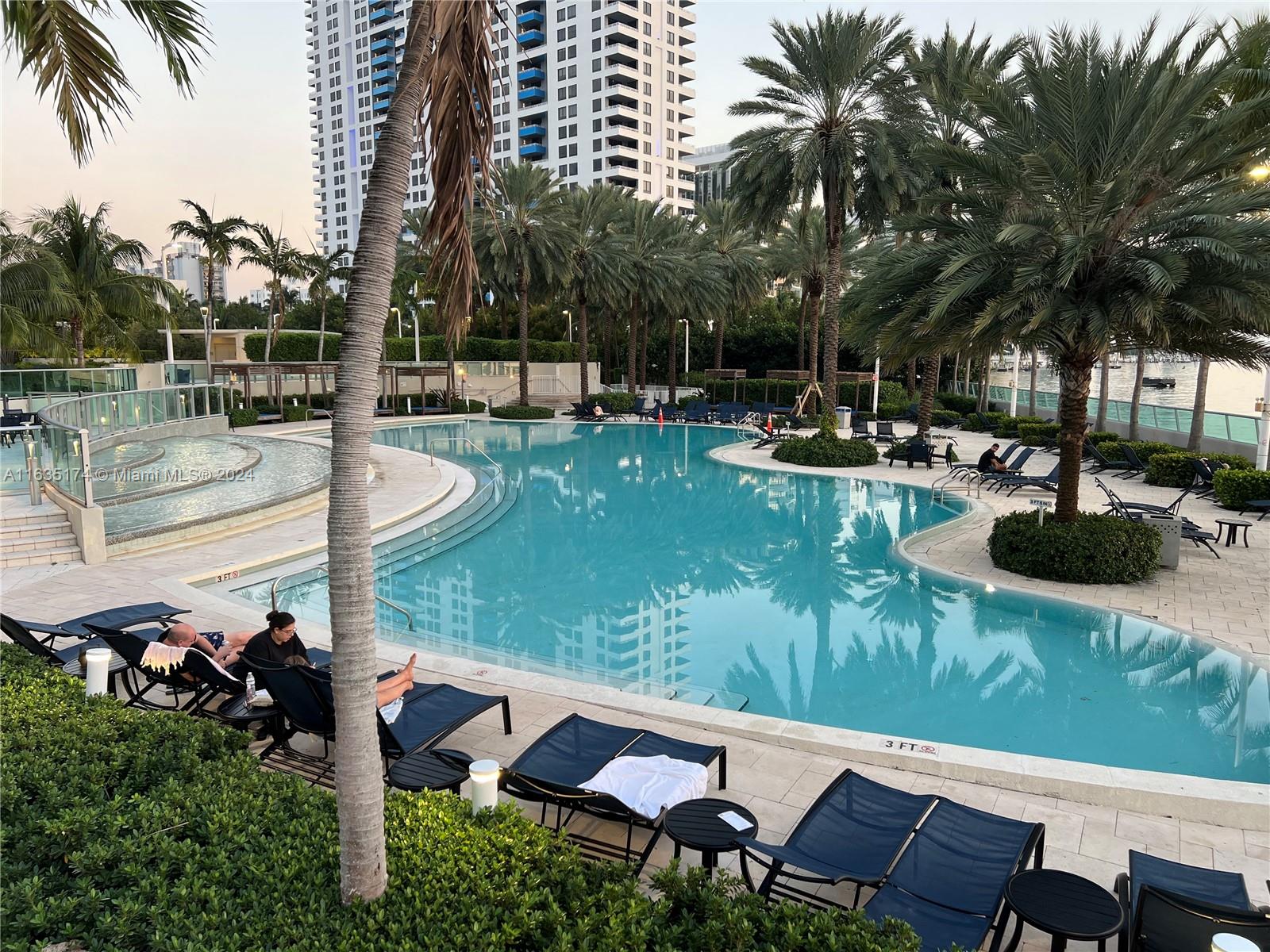 A swimming pool with lounge chairs and palm trees sits in front of a high-rise building — 1500 Bay Rd # 522S, Miami Beach FL 33139, MIAMI BEACH, FL