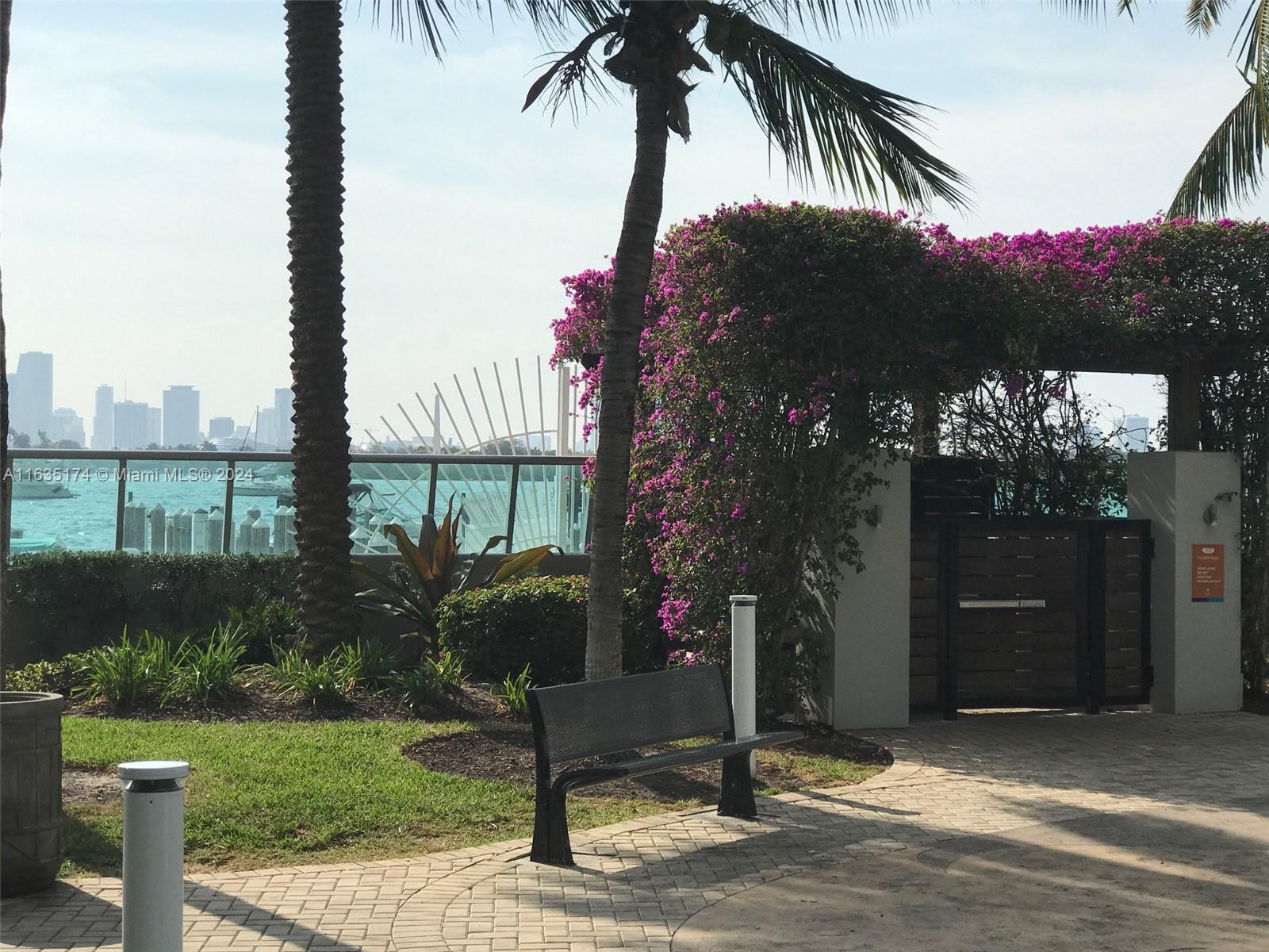 A park bench sits on a paved walkway near a palm tree and flowering bougainvillea trellis — 1500 Bay Rd # 522S, Miami Beach FL 33139, MIAMI BEACH, FL