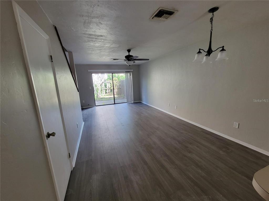 An empty living room features gray wood-look flooring, a ceiling fan, and sliding glass doors — 3625 NE 20TH PLACE, OCALA, FL