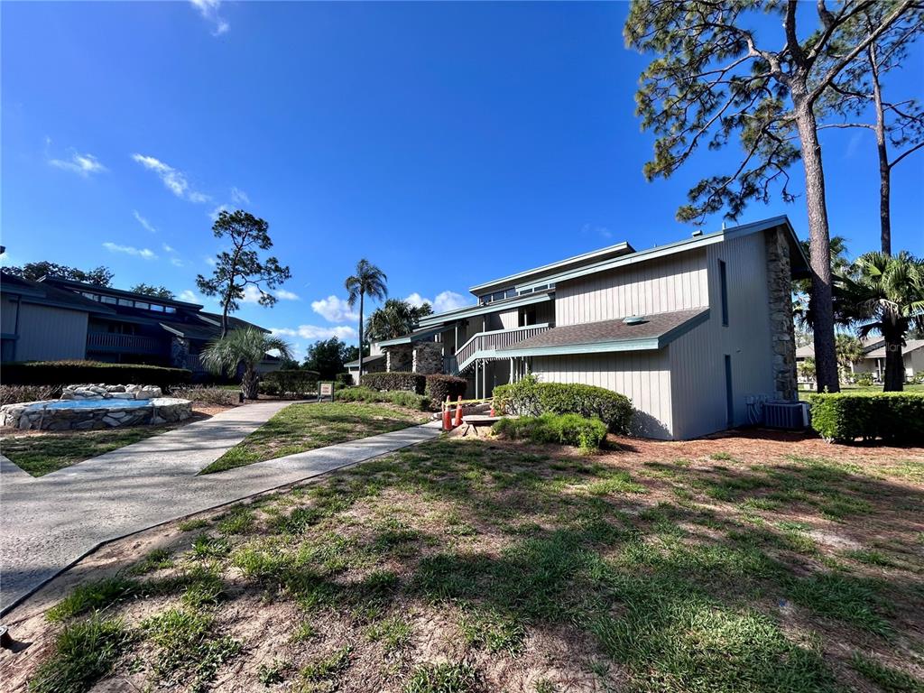 A multi-story apartment building with light-colored siding stands near a stone fountain and trees — 2068 CORNER LAKE DRIVE, HAINES CITY, FL