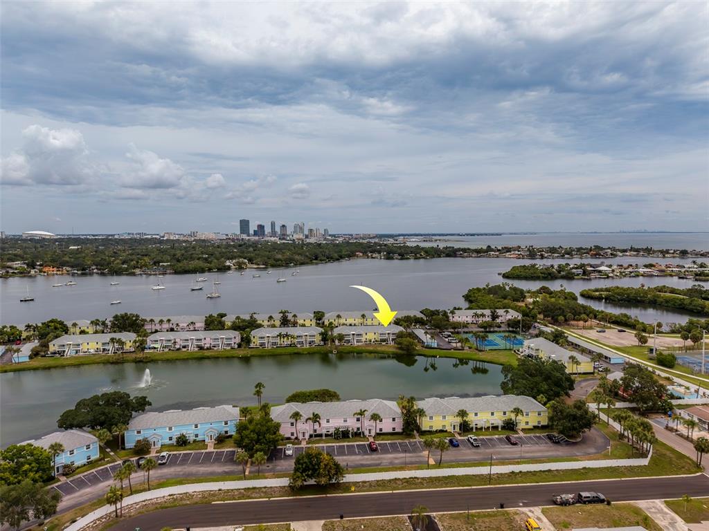 An aerial view shows multi-story apartment buildings situated along a lake with a city skyline — 222 POMPANO DRIVE SE UNIT H, ST PETERSBURG, FL