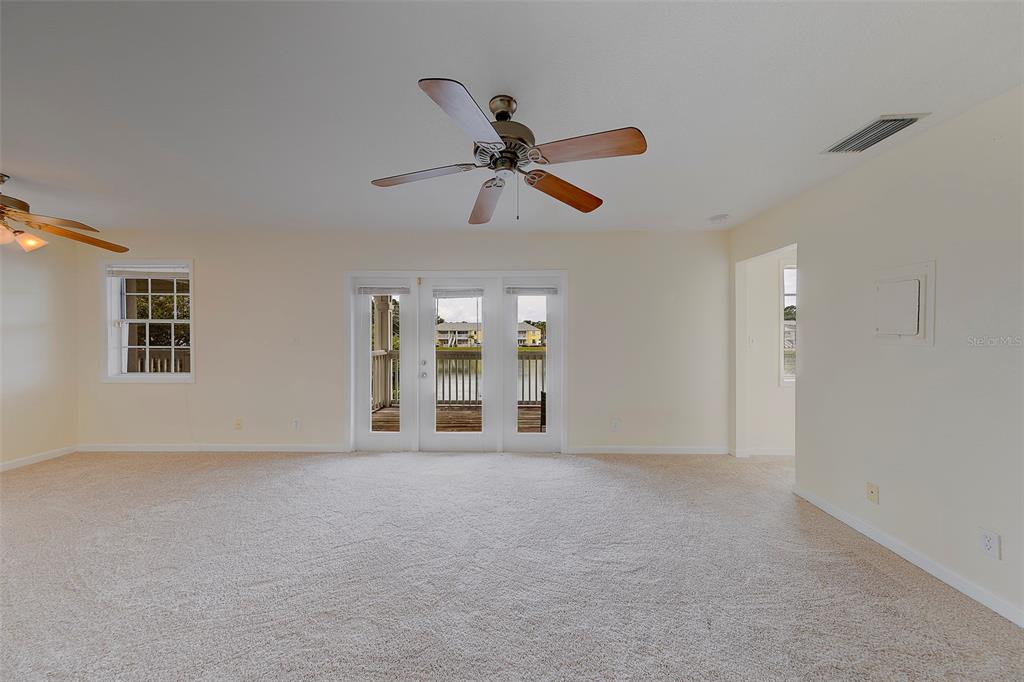 A carpeted living room features two ceiling fans, a window, and glass doors to a balcony — 222 POMPANO DRIVE SE UNIT H, ST PETERSBURG, FL