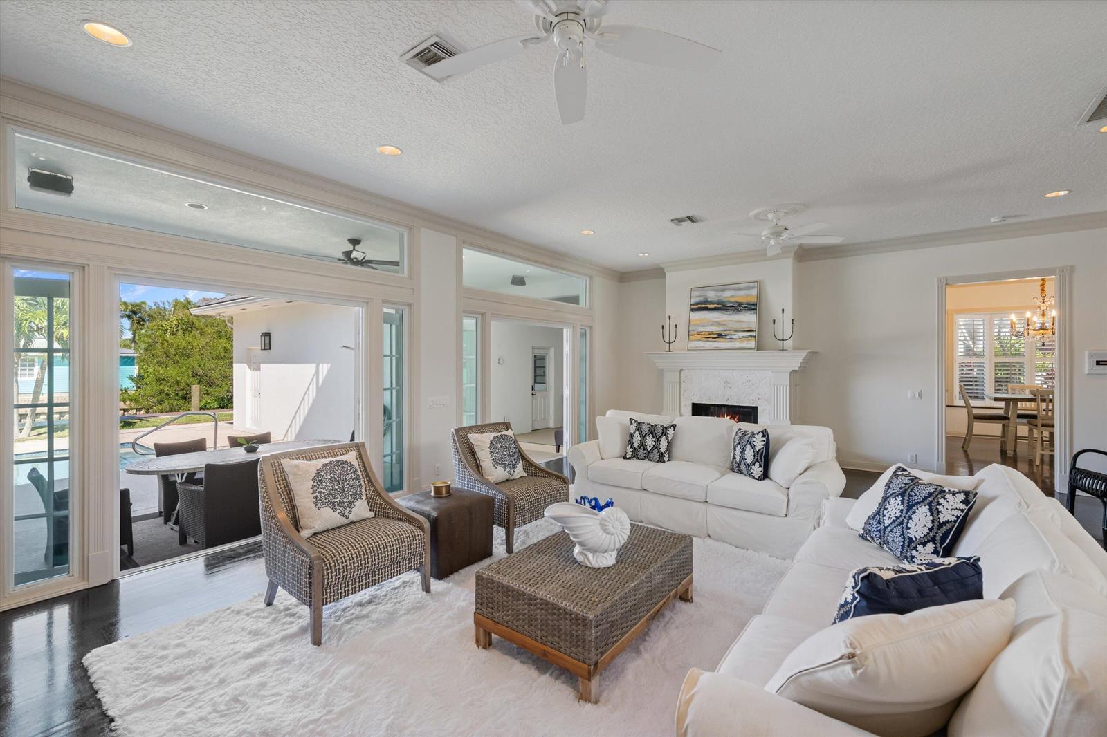 A bright living room features white sofas, patterned armchairs, a fireplace, and large sliding glass doors — 401 Center Street, Jupiter FL 33458, JUPITER, FL