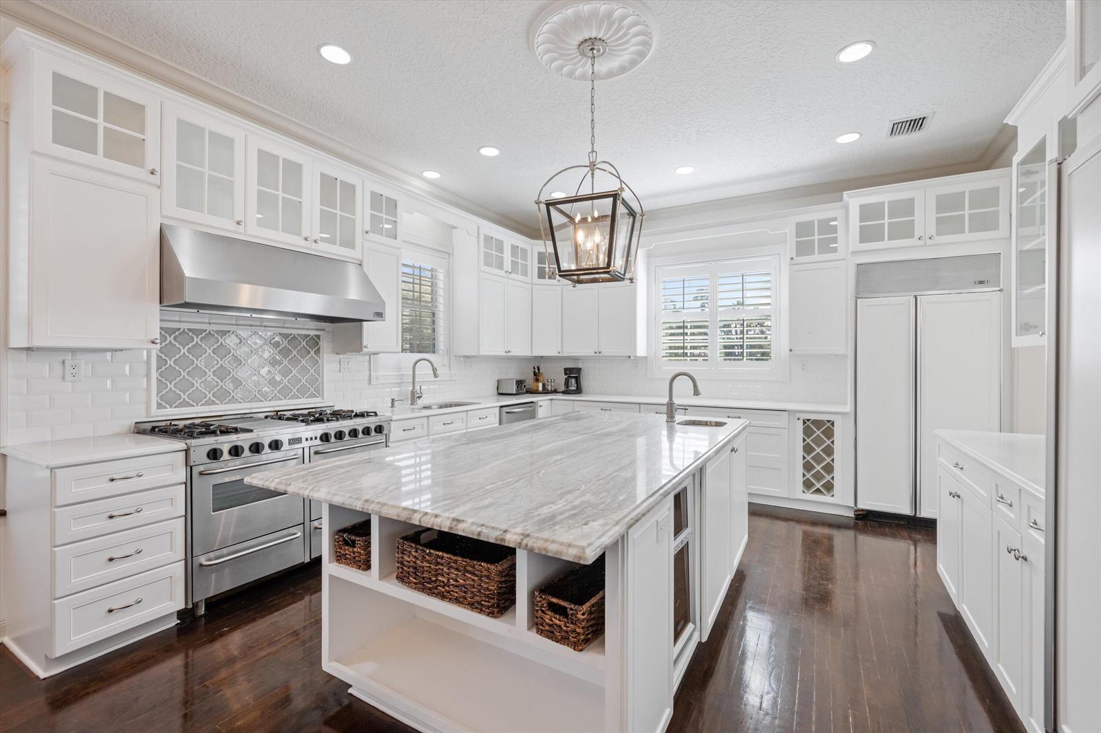 A white kitchen features a large marble-topped island, stainless steel appliances, and dark hardwood floors — 401 Center Street, Jupiter FL 33458, JUPITER, FL