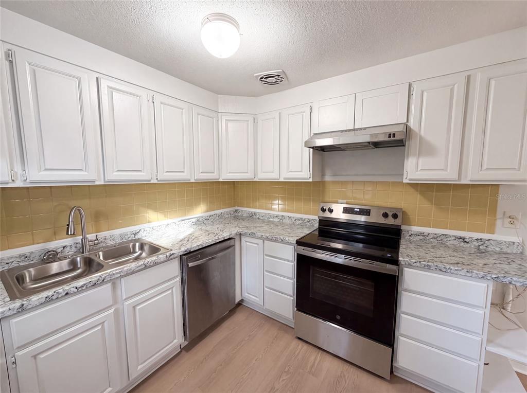 A kitchen with white cabinets, granite-look countertops, stainless steel appliances, and yellow tile backsplash — 1436 ALABAMA AVENUE, HOLLY HILL, FL