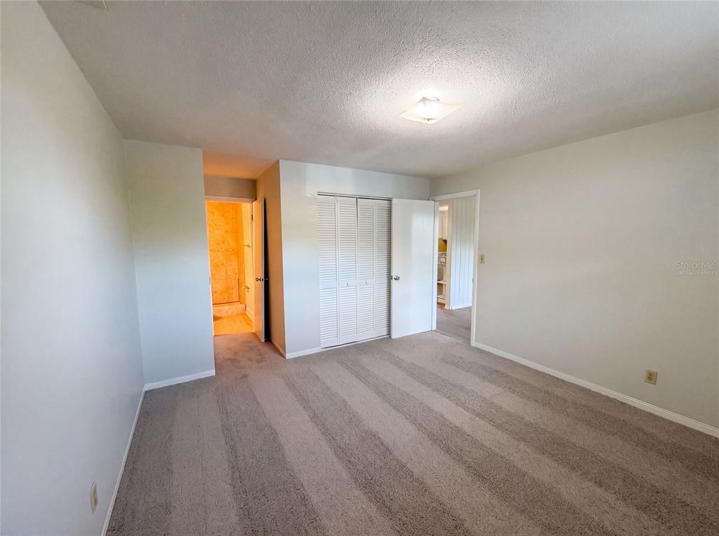 An empty bedroom features light gray walls, beige carpet, a closet with louvered doors, and doorways — 1436 ALABAMA AVENUE, HOLLY HILL, FL