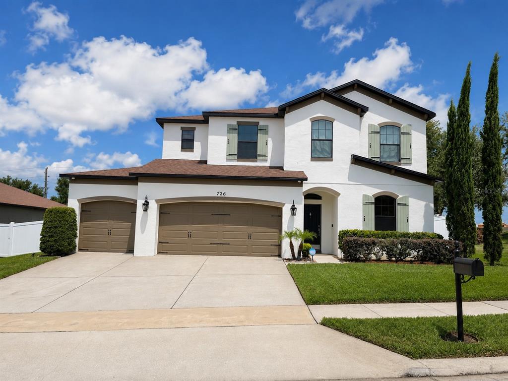A two-story white stucco house with a three-car garage and green shutters — 726 WOODS LANDING DRIVE, MINNEOLA, FL