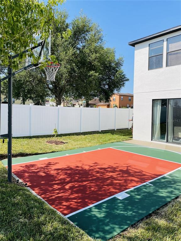 A backyard features a basketball court with a hoop next to a white house — 726 WOODS LANDING DRIVE, MINNEOLA, FL