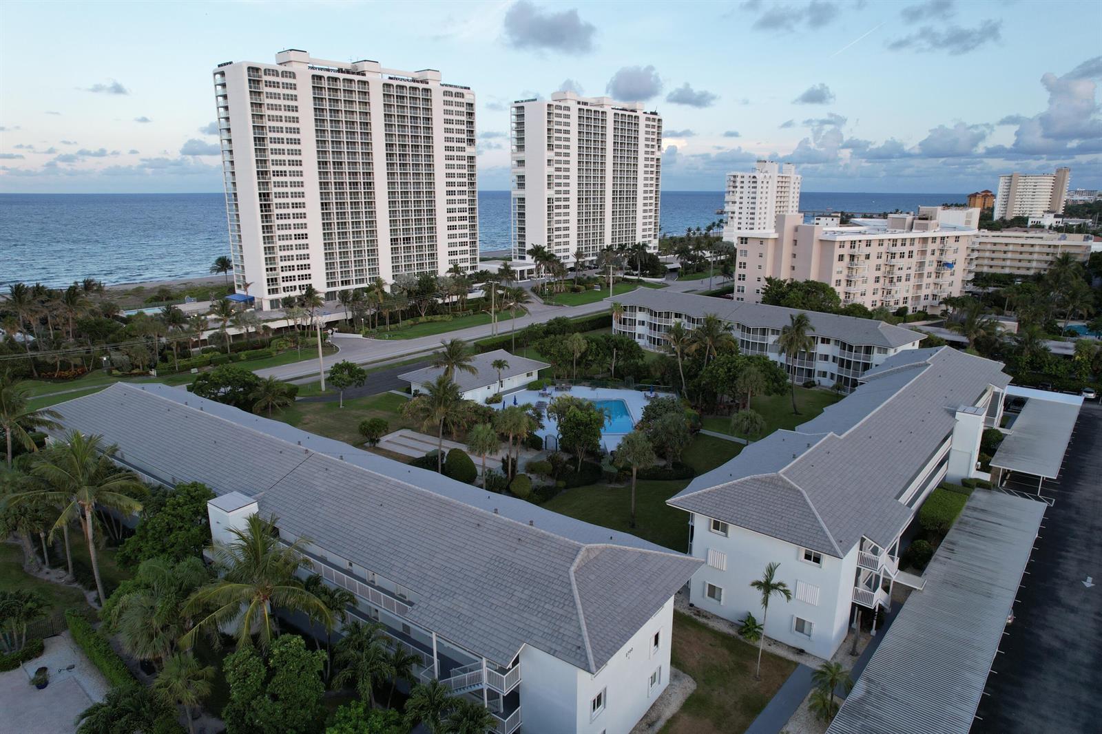 An aerial view shows low-rise apartment buildings surrounding a pool near high-rise oceanfront towers — 2700 Banyan Road # 3, Boca Raton FL 33432, BOCA RATON, FL