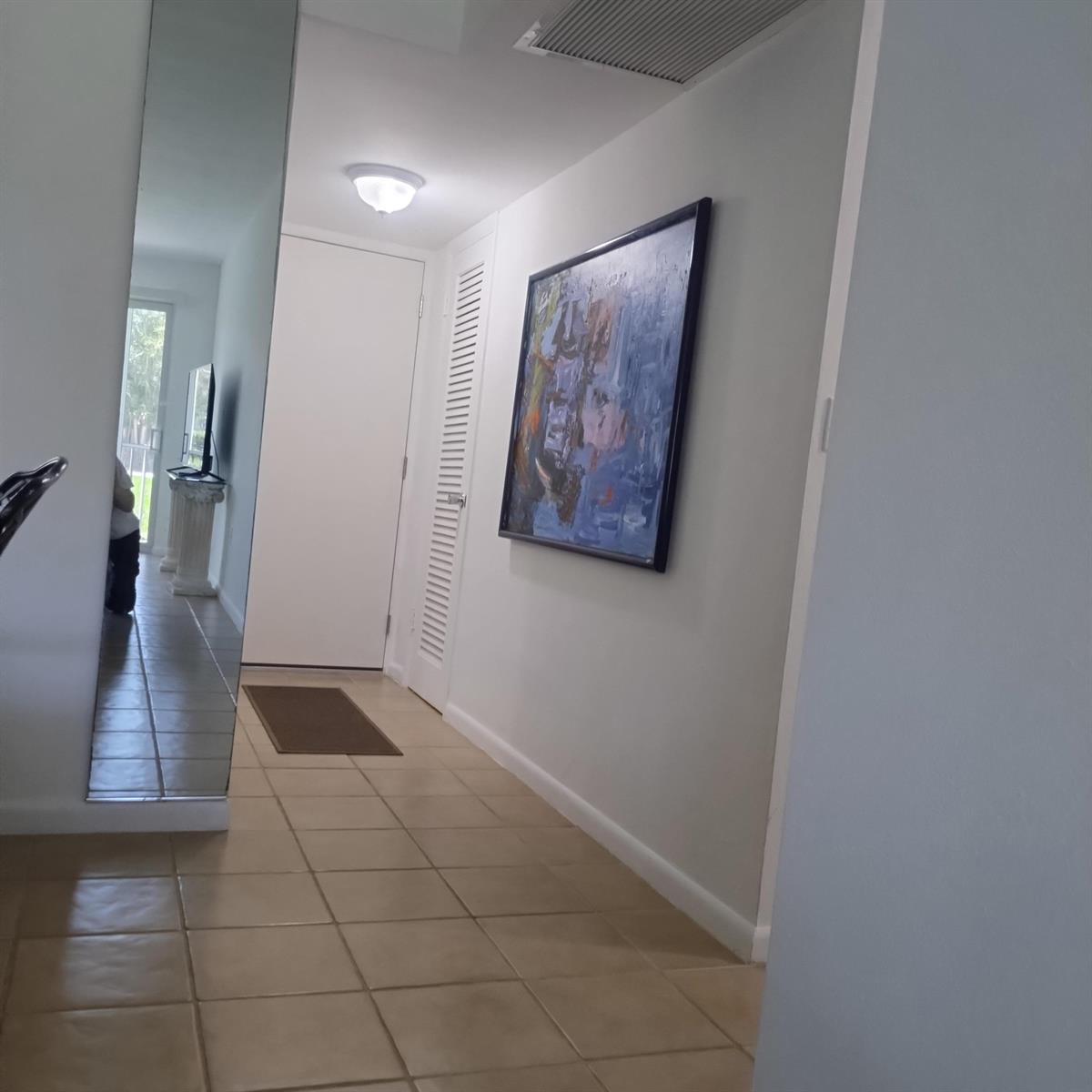 A hallway with beige tile flooring, a large mirror, and an abstract painting on the wall — 2700 Banyan Road # 3, Boca Raton FL 33432, BOCA RATON, FL