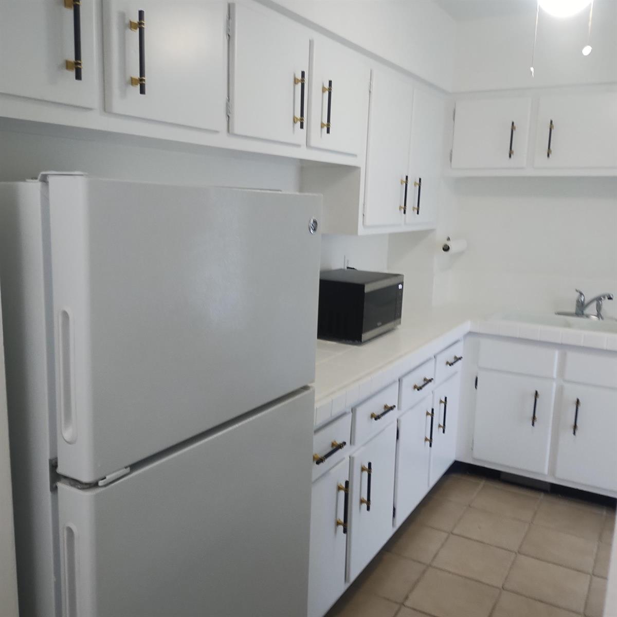 A kitchen features white cabinets with gold hardware, a white refrigerator, and tiled flooring — 2700 Banyan Road # 3, Boca Raton FL 33432, BOCA RATON, FL