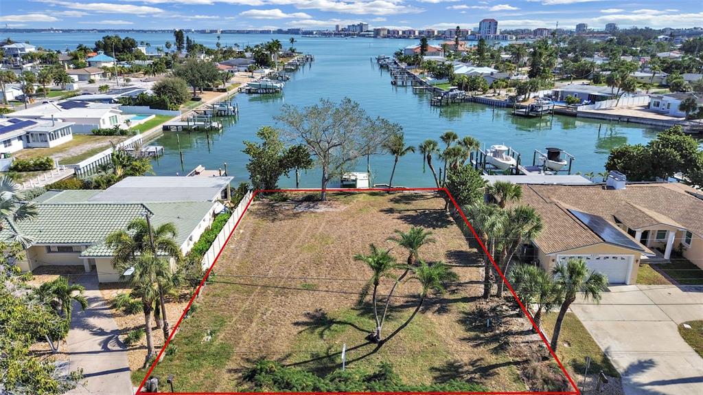An aerial view shows a vacant waterfront lot outlined in red between two residential houses — 4031 POINSETTIA DRIVE, ST PETE BEACH, FL