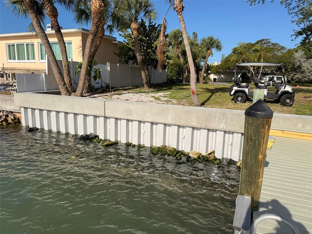 A concrete seawall borders a waterfront lot with palm trees and a parked golf cart — 4031 POINSETTIA DRIVE, ST PETE BEACH, FL