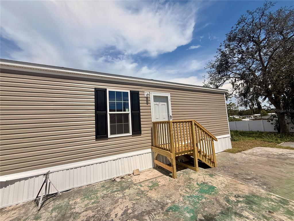 A tan mobile home exterior features a wooden staircase leading to a white entry door — 9024 KOSIMO STREET, NEW PORT RICHEY, FL