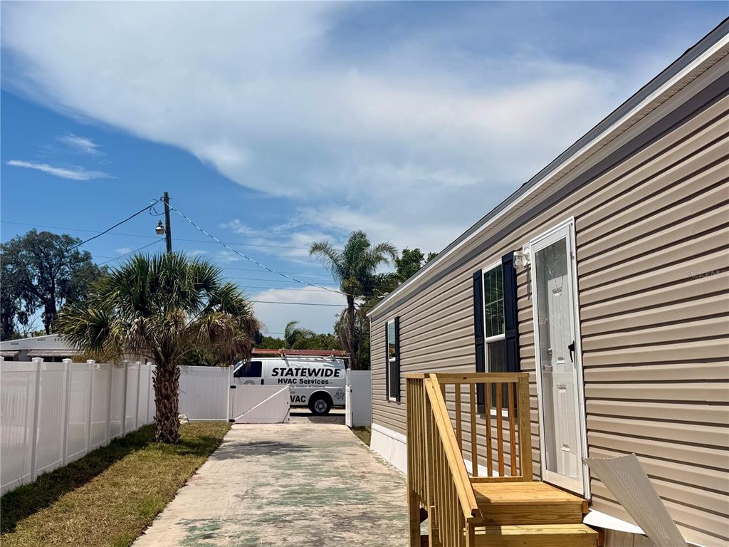 A tan mobile home with a wooden staircase sits beside a driveway and white fence — 9024 KOSIMO STREET, NEW PORT RICHEY, FL