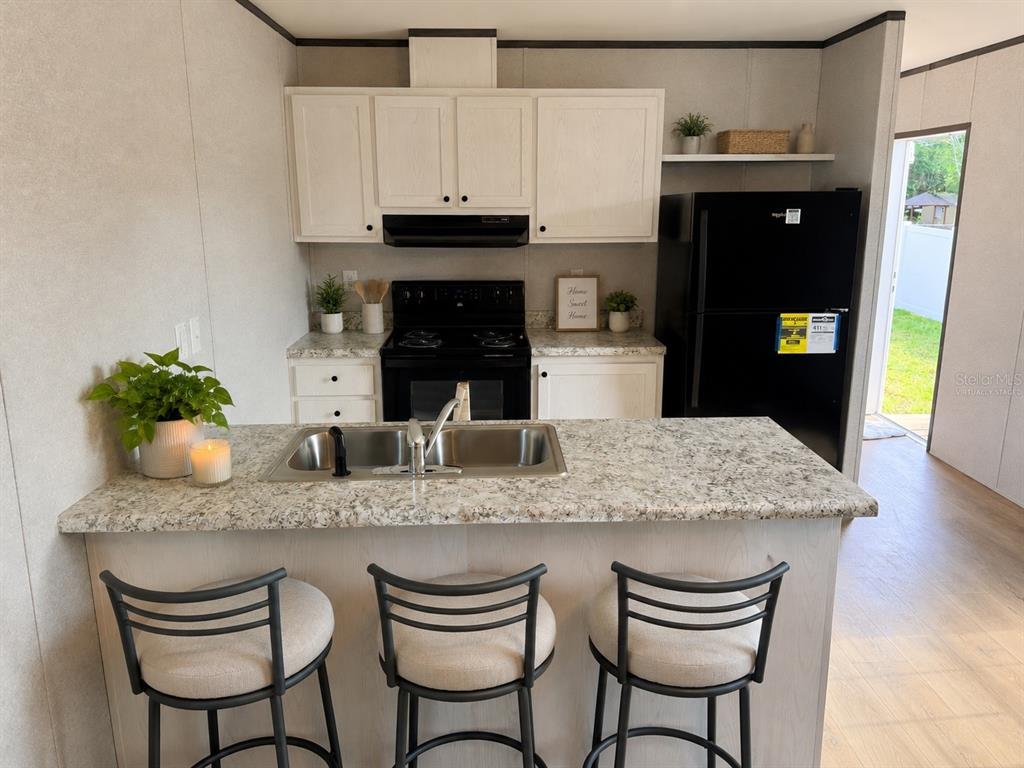 A kitchen features white cabinets, a granite countertop island with a sink, and black appliances — 9024 KOSIMO STREET, NEW PORT RICHEY, FL