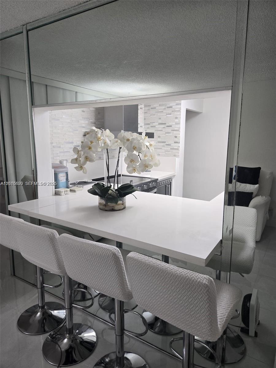 A white breakfast bar with three stools sits in front of a mirrored kitchen pass-through — 9410 Live Oak Pl # 103, Davie FL 33324, DAVIE, FL