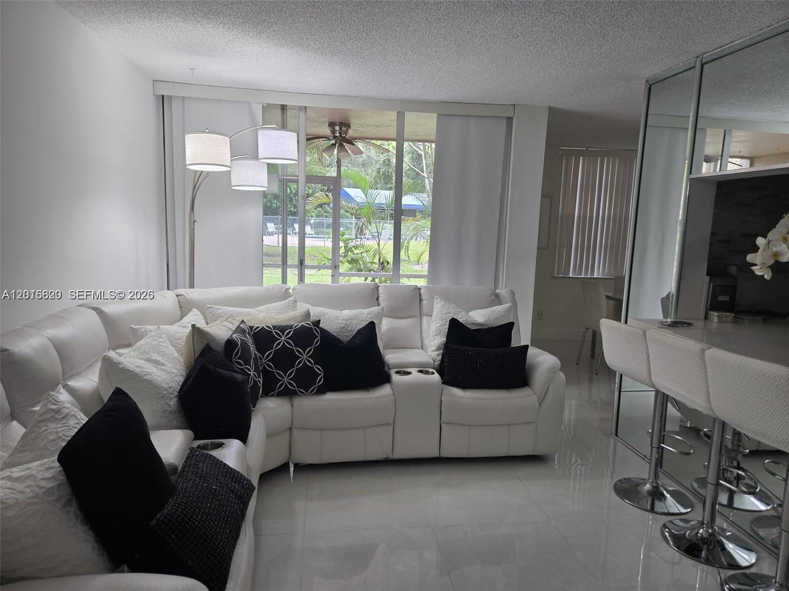 A white sectional sofa sits in a living room with tile floors and a patio view — 9410 Live Oak Pl # 103, Davie FL 33324, DAVIE, FL