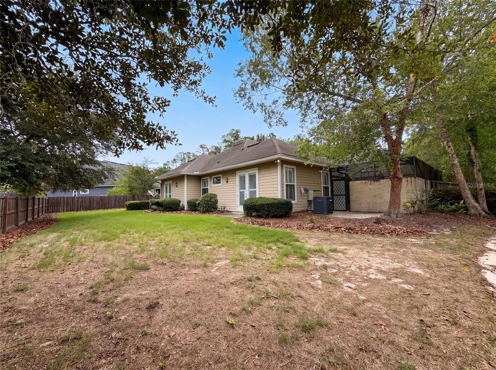 The exterior of a tan house features a grassy backyard, a patio, and mature trees — 13478 NW 9TH ROAD, NEWBERRY, FL