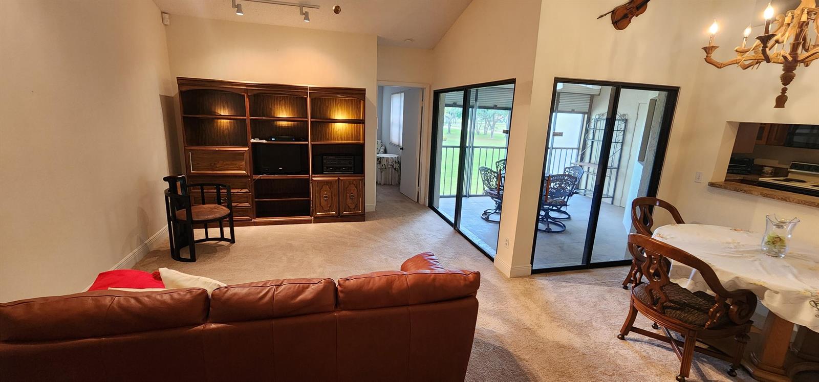 A living room with a large wooden wall unit, leather sofa, and sliding glass doors — 6043 Parkwalk Drive, Boynton Beach FL 33472, BOYNTON BEACH, FL