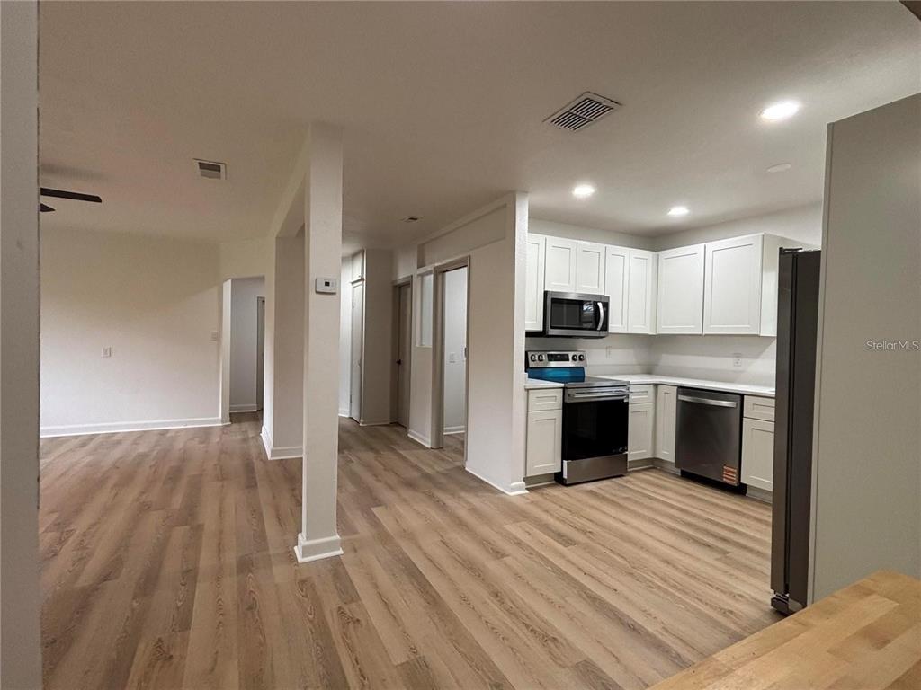 A kitchen with white cabinets and stainless steel appliances opens to a living area — 2035 VOLTAIRE STREET, LAKELAND, FL