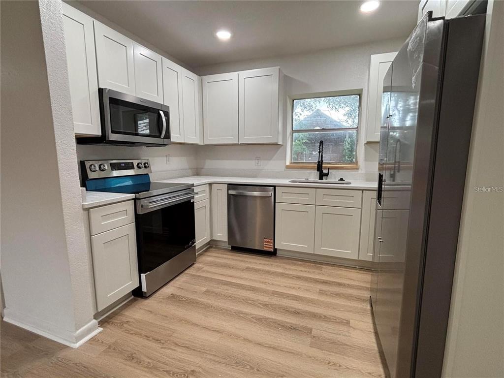 A kitchen features white cabinets, stainless steel appliances, light wood-look flooring, and a window — 2035 VOLTAIRE STREET, LAKELAND, FL