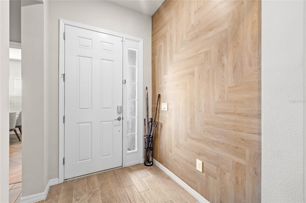 An entryway features a white front door, light wood-look flooring, and a herringbone-patterned wood wall — 2146 RIDGE POINTE LANE, CLERMONT, FL