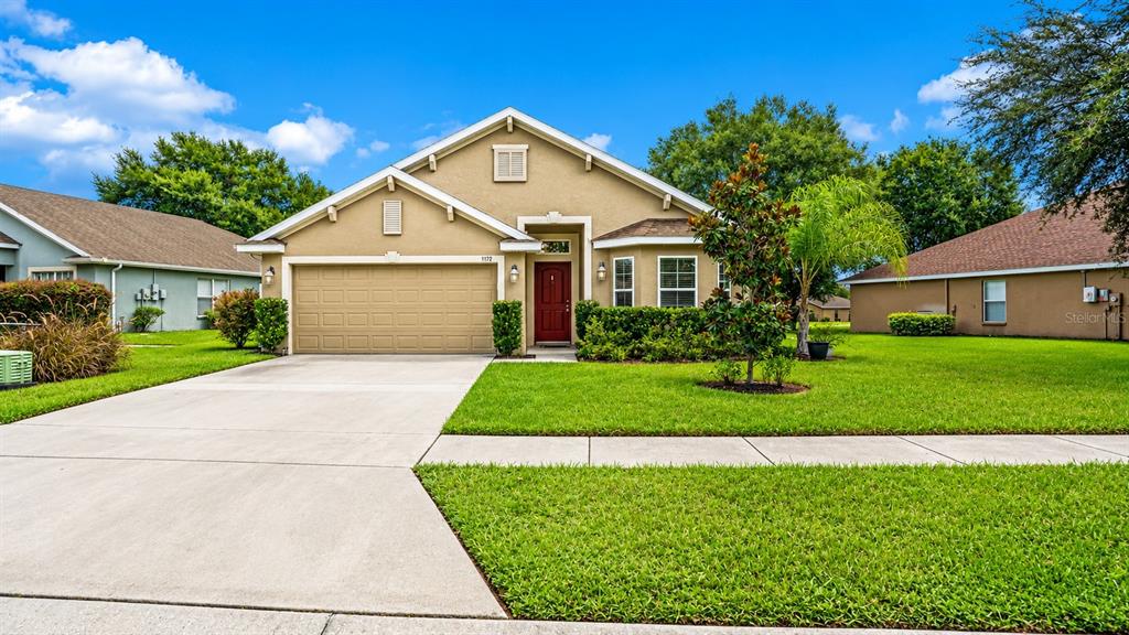 A single-story suburban house with a tan exterior, a two-car garage, and a green lawn — 7172 SHERMAN HILLS BOULEVARD, BROOKSVILLE, FL