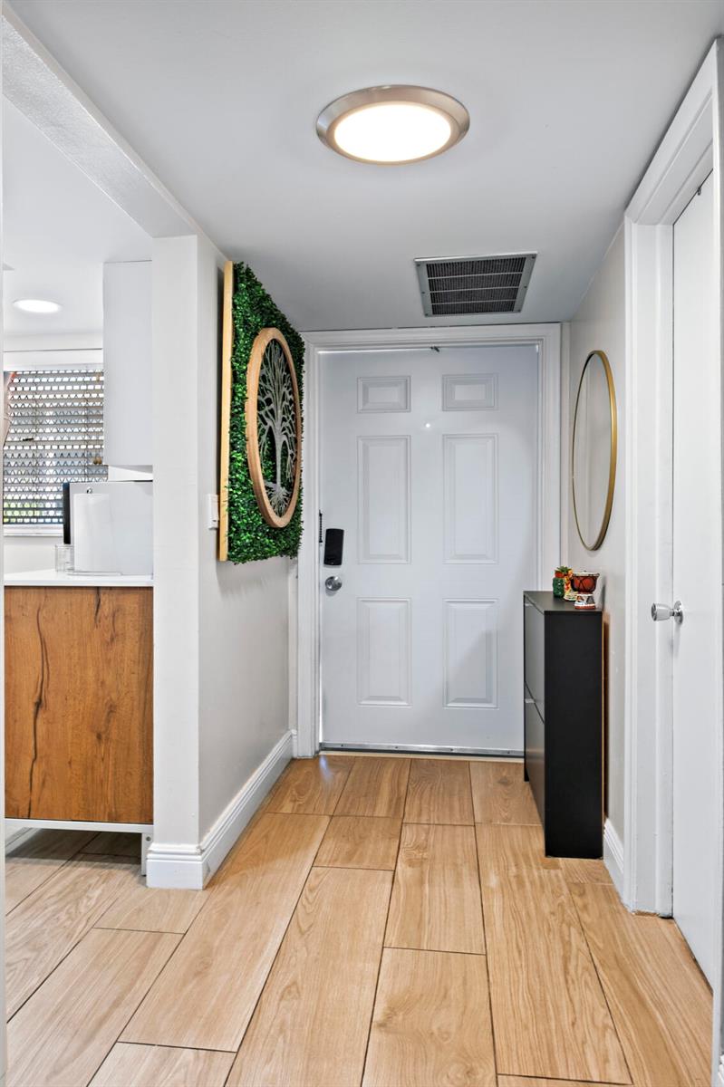 An entryway features light wood-look tile flooring, a white front door, and a wall-mounted tree art piece — 899 SE 2nd Avenue # 116, Deerfield Beach FL 33441, DEERFIELD BEACH, FL