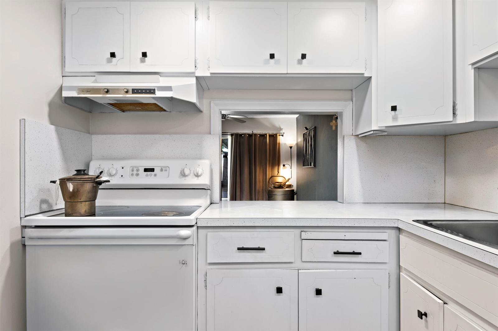 A kitchen features white cabinets, white countertops, a white stove, and a pass-through window — 899 SE 2nd Avenue # 116, Deerfield Beach FL 33441, DEERFIELD BEACH, FL