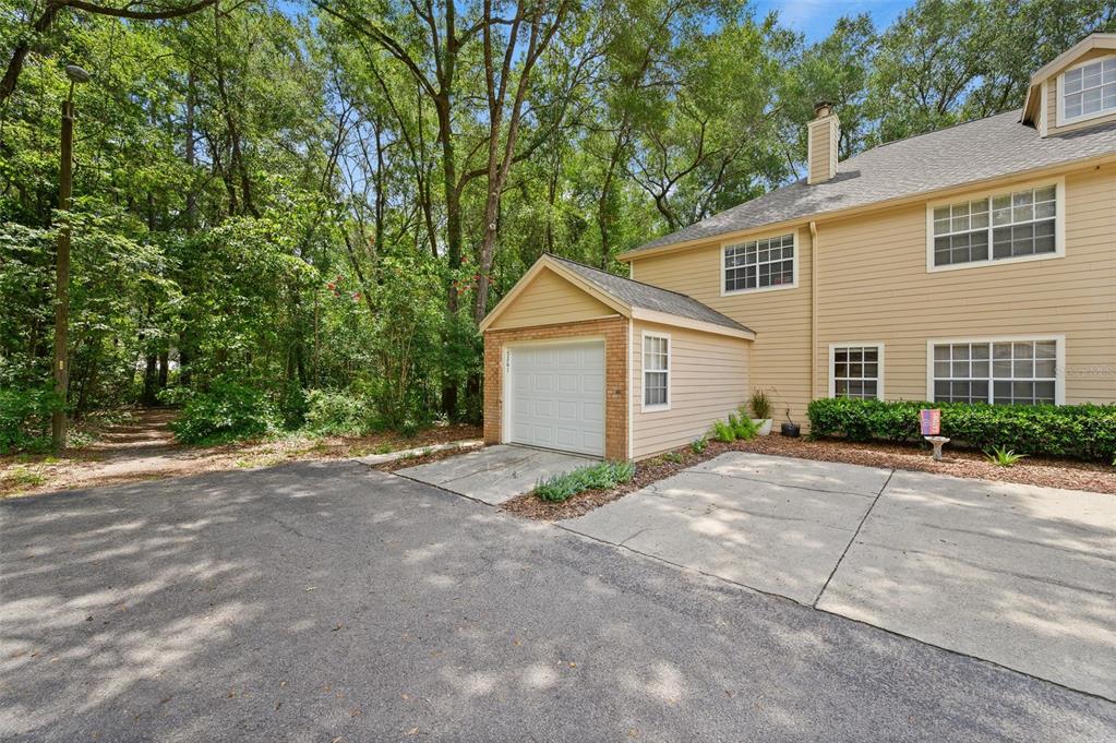 A tan two-story house features a single-car garage, concrete driveway, and surrounding wooded area — 5261 SW 97TH DRIVE, GAINESVILLE, FL