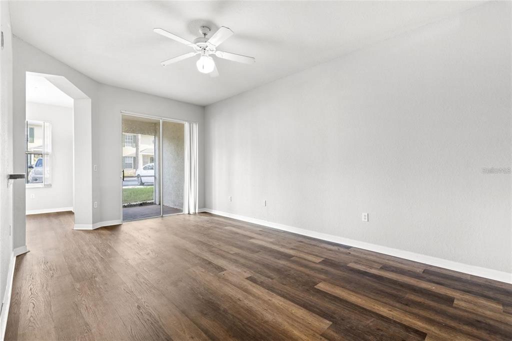 An empty living room features wood-look flooring, white walls, a ceiling fan, and sliding glass doors — 5009 SUNRIDGE PALMS DRIVE UNIT 203, TAMPA, FL