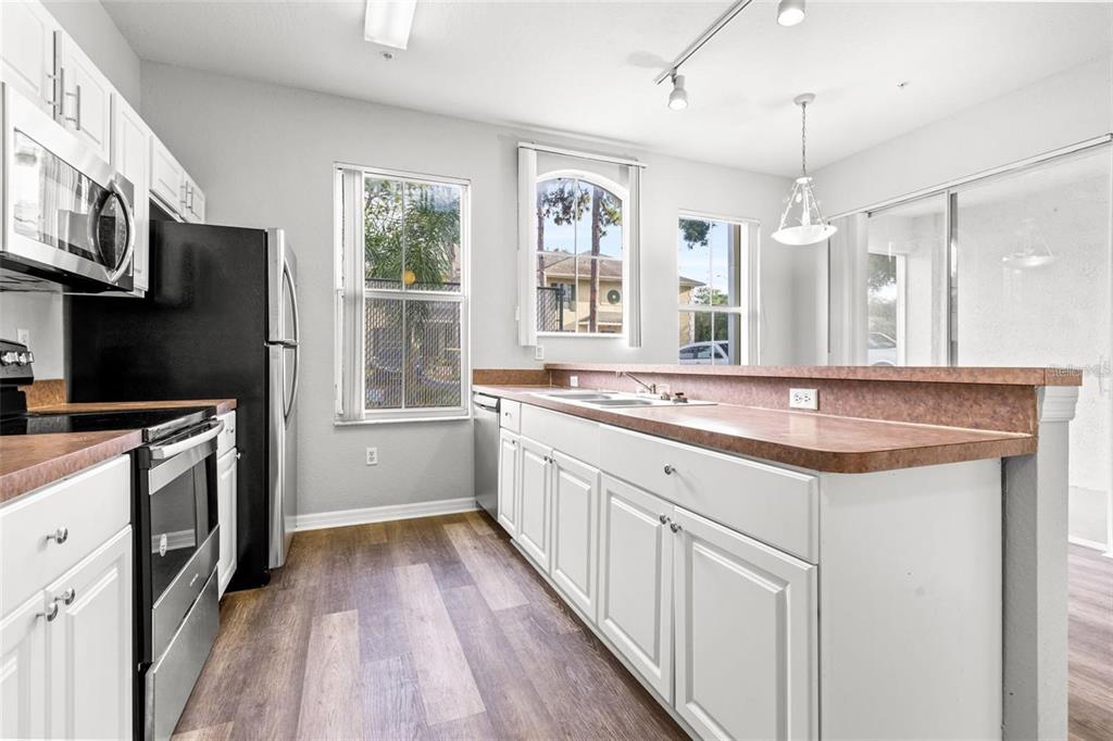 A kitchen features white cabinetry, a brown countertop, stainless steel appliances, and wood-look flooring — 5009 SUNRIDGE PALMS DRIVE UNIT 203, TAMPA, FL