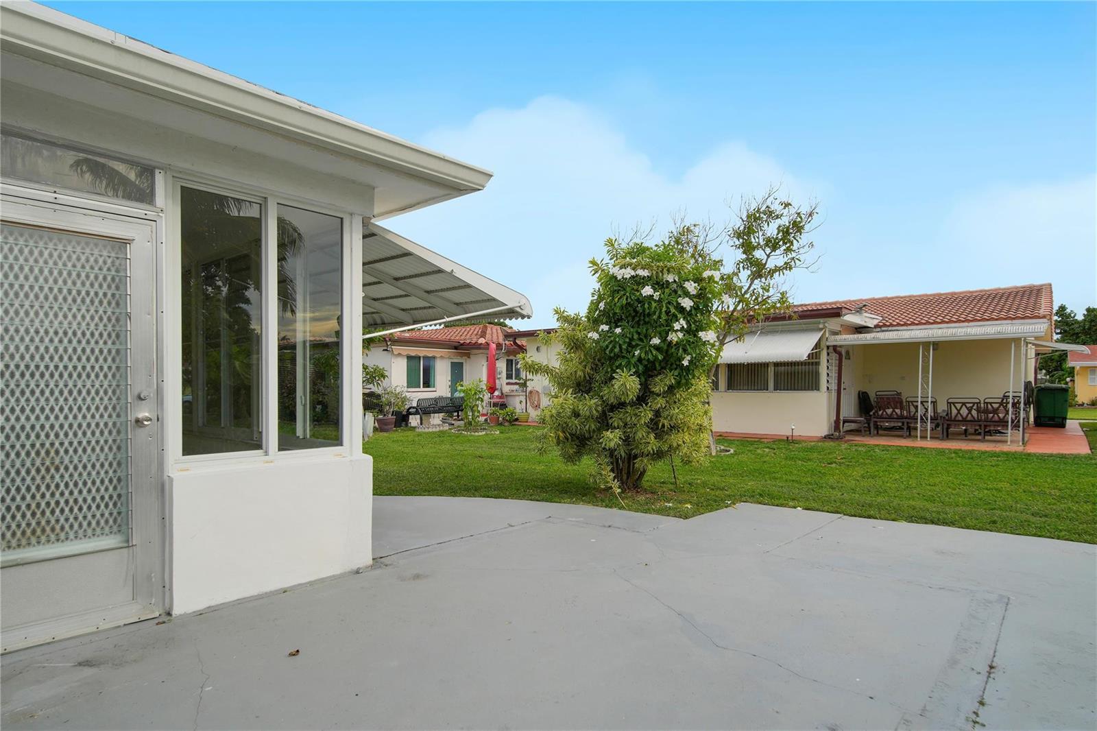 A backyard view featuring a concrete patio, a grassy lawn, and neighboring single-story houses — 4510 NW 49th Drive, Tamarac FL 33319, TAMARAC, FL
