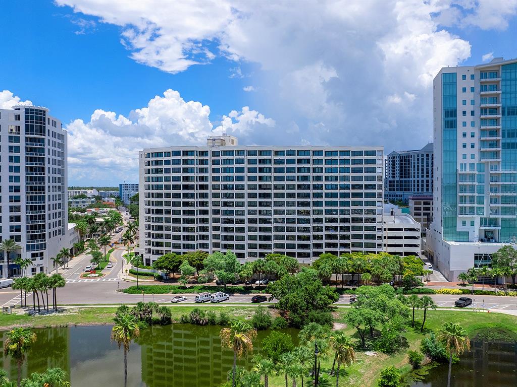 An exterior view of a large multi-story apartment building situated near a pond and street — 1255 N GULFSTREAM AVENUE UNIT 205, SARASOTA, FL