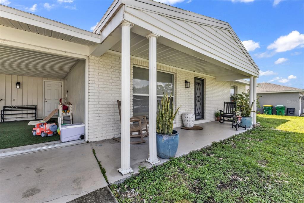 A white brick house exterior features a covered front porch with columns and a carport — 394 KOSTNER STREET, PORT CHARLOTTE, FL