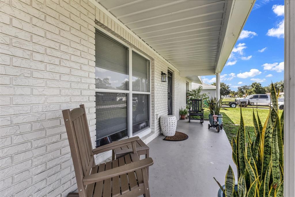 A covered front porch features white brick walls, a concrete floor, and wooden rocking chairs — 394 KOSTNER STREET, PORT CHARLOTTE, FL