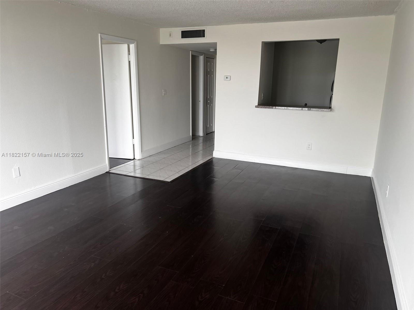 An empty room features dark wood flooring, a tiled entryway, and a kitchen pass-through window — 498 NW 165th St Rd # D303, Miami FL 33169, MIAMI, FL